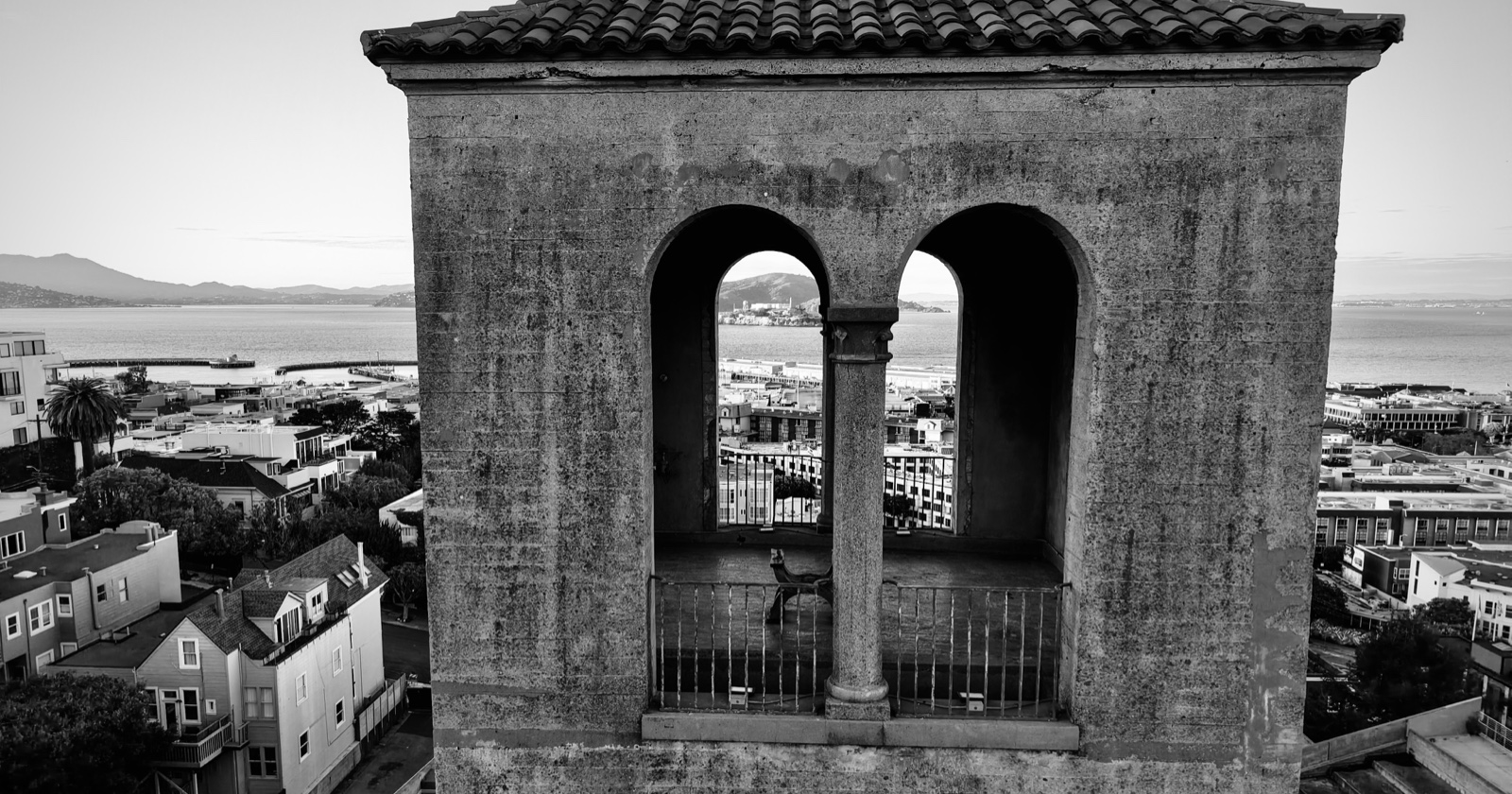 Black-and-white aerial view of the former San Francisco Art Institute with the Bay visible through its arches.
